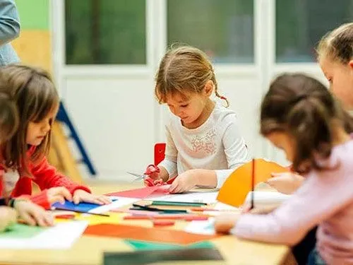 Little girls at the desk in the classroom cutting out paper to make an origami mouse.