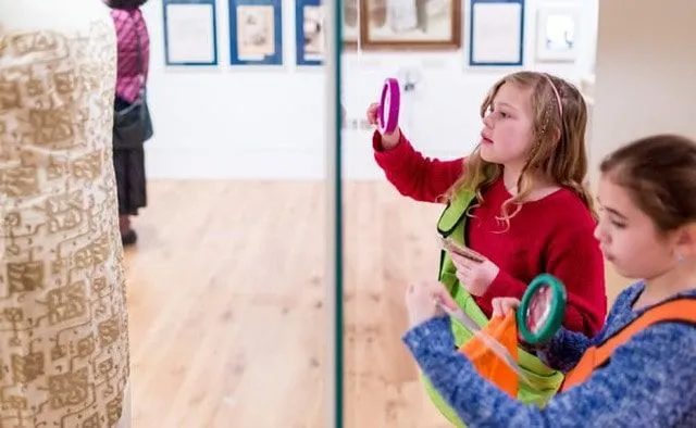 Two girls holding up magnifying glasses to an exhibit a The Jewish Museum.