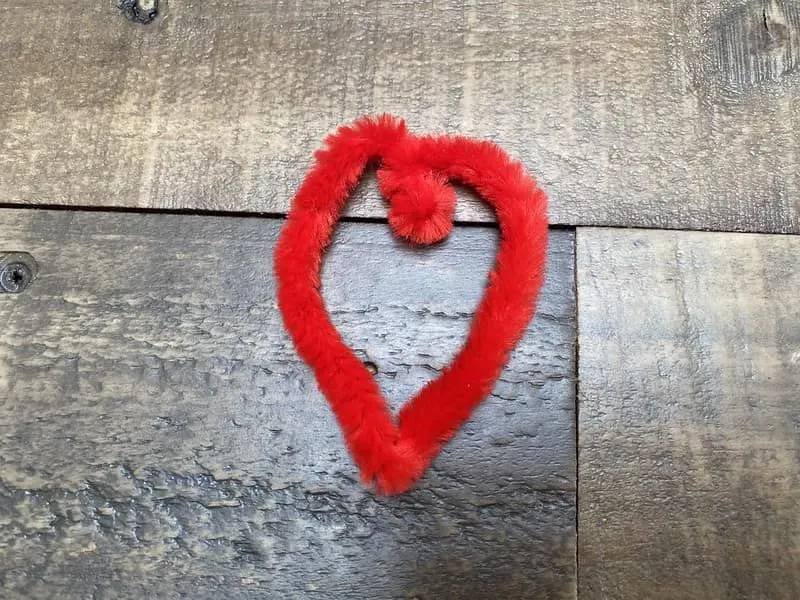 Red pipe cleaner shaped like a heart on the wooden floor.