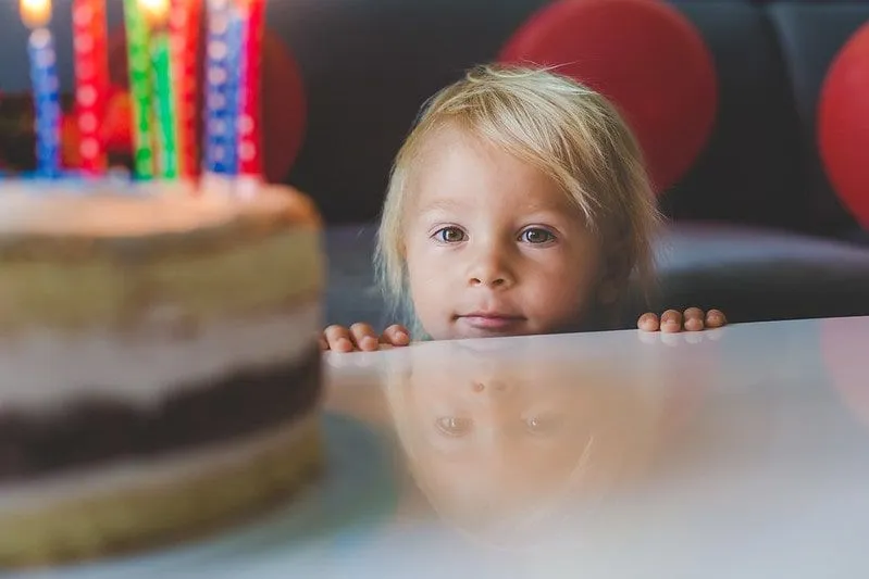 Toddler standing at the edge of the table peeking up at a birthday cake.