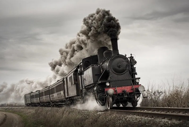 A Victorian steam train moving along the railways, producing black steam as it goes.
