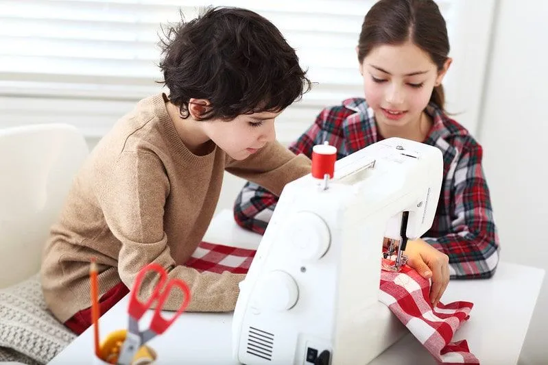 Two children using a sewing machine together.