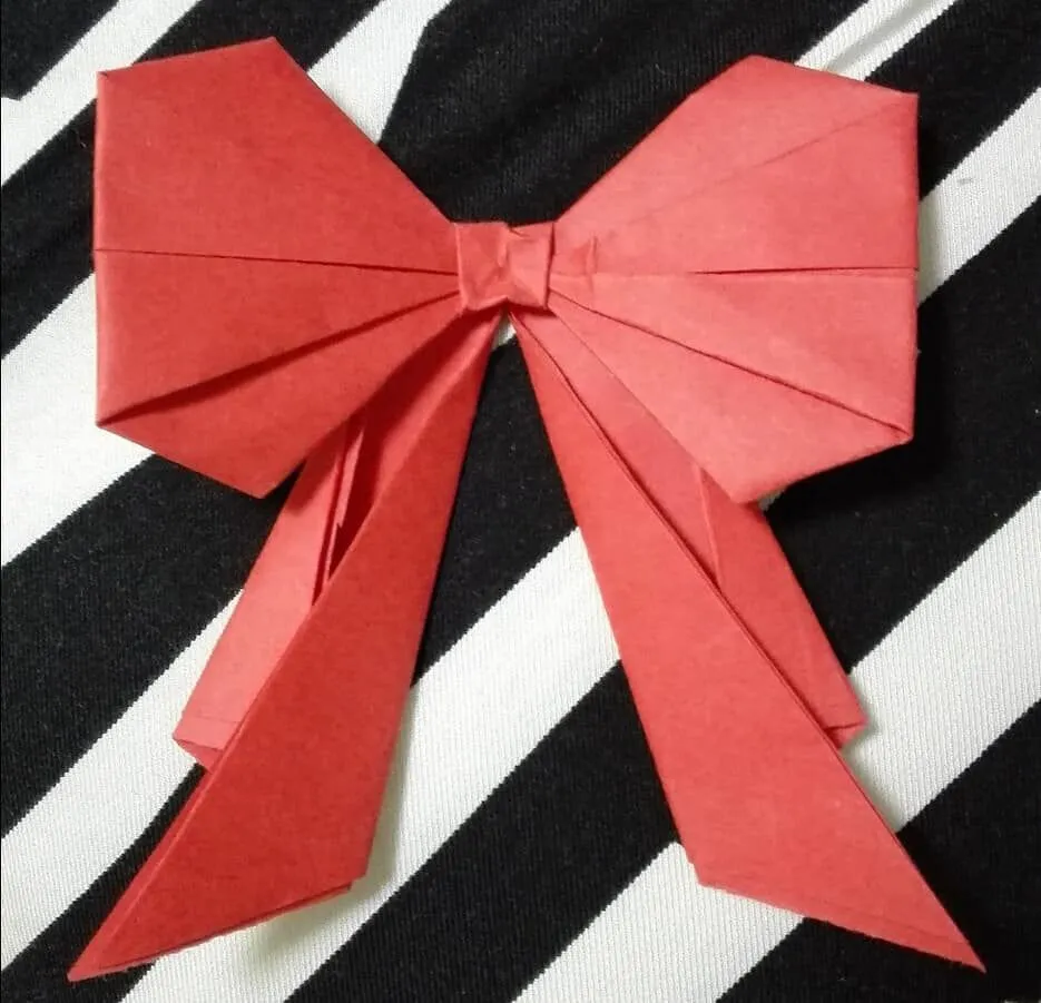 A red origami bow against a black and white striped background.