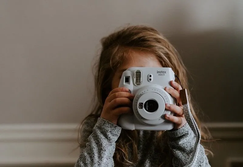 Little girl taking a photo with a polaroid camera.