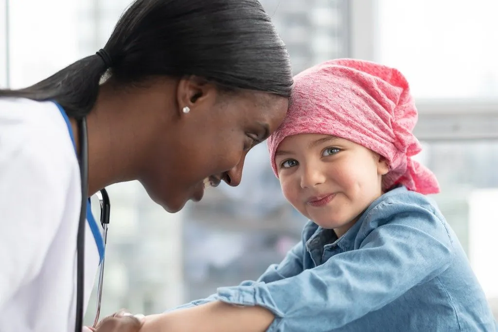 Sweet little girl, wearing a red bandana on her head, smiling with a hospital nurse.