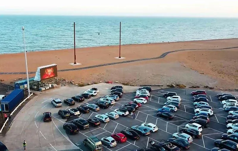 Cars parked up to watch a movie on a big screen just by the seafront.