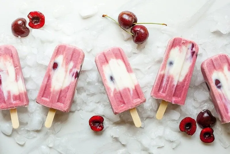 Fruity cherry and yoghurt ice lollies laid out next to each other on ice.