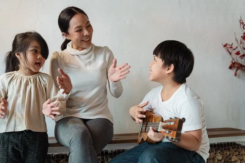 Little boy playing the ukulele for his mum and sister who are clapping along.