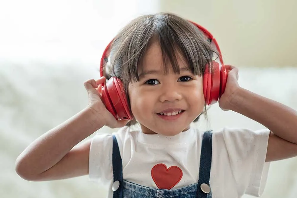 Little girl listening to music through red heaphones.