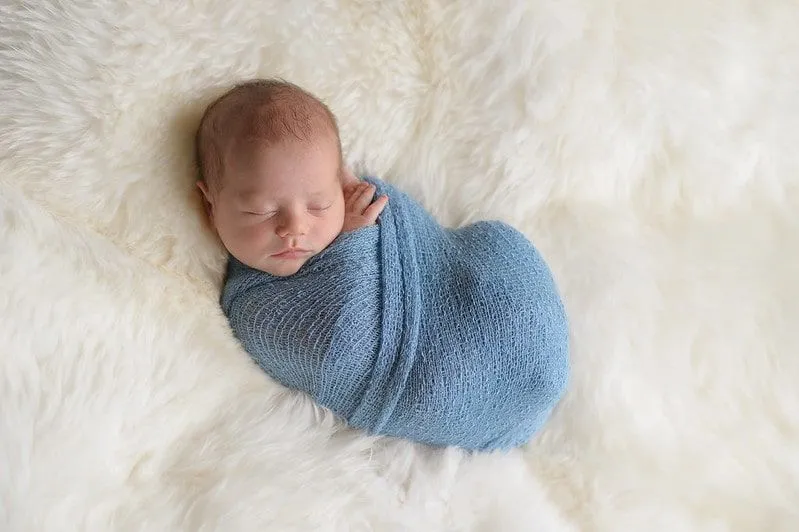 Sleeping baby boy swaddled in a blue blanket.