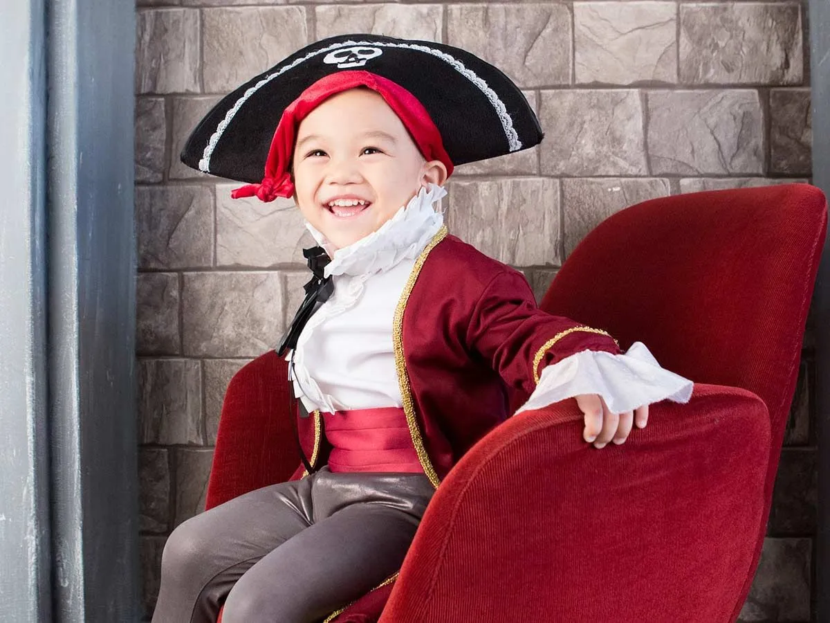 Young boy dressed as a pirate sitting on a red velvet chair.