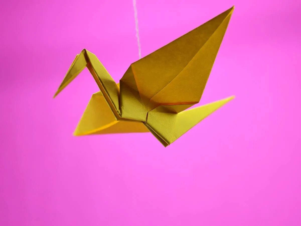 Golden origami bird with wings spread in front of a pink background.