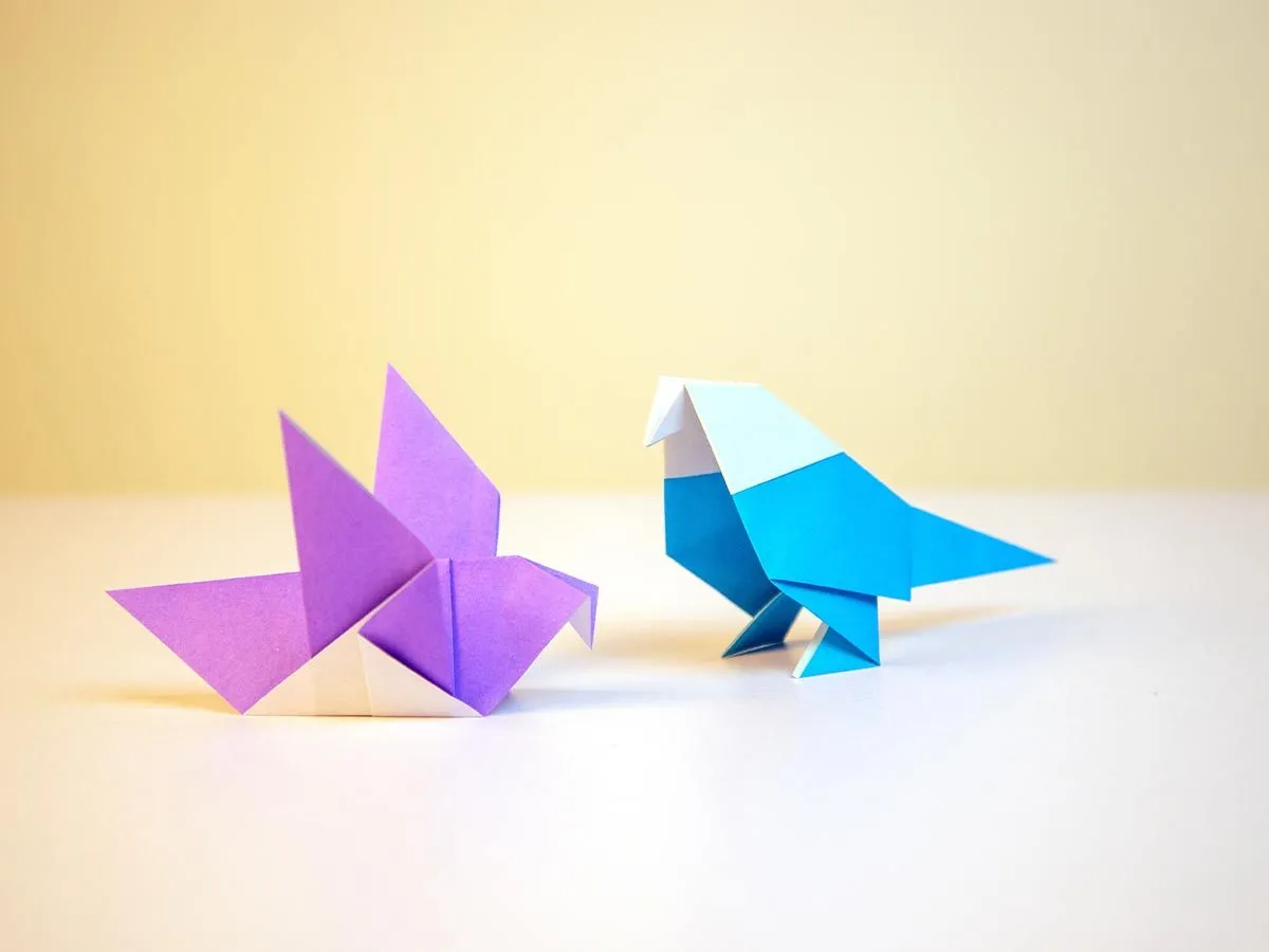 A purple and a blue origami parrot on a white table.