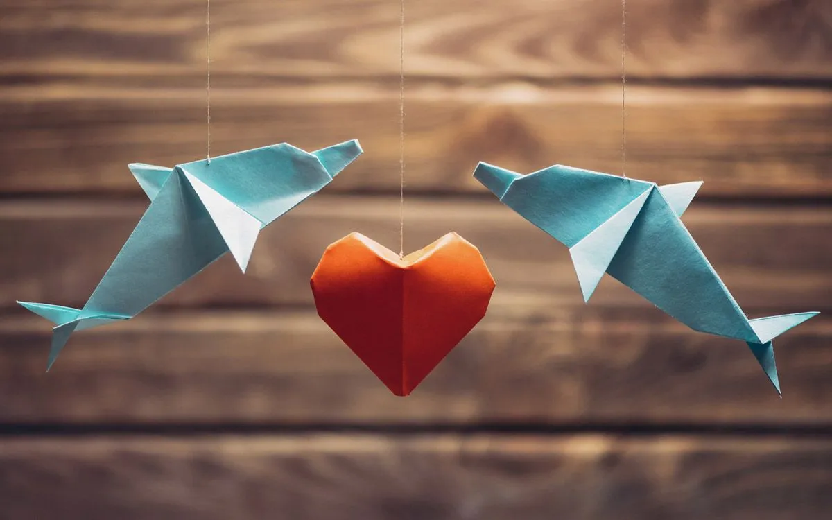 Two origami dolphins hanging on a string with an origami heart hanging in between them.