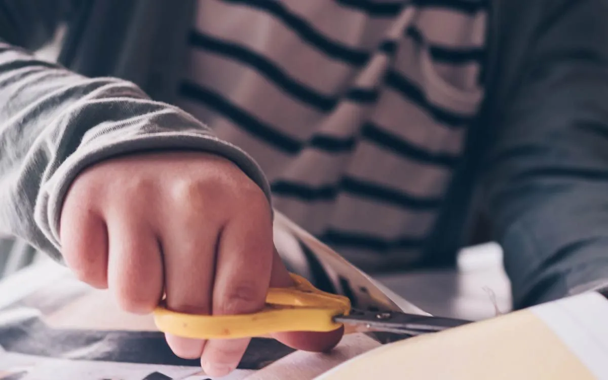 Close up of a child cutting paper to make an origami dolphin.