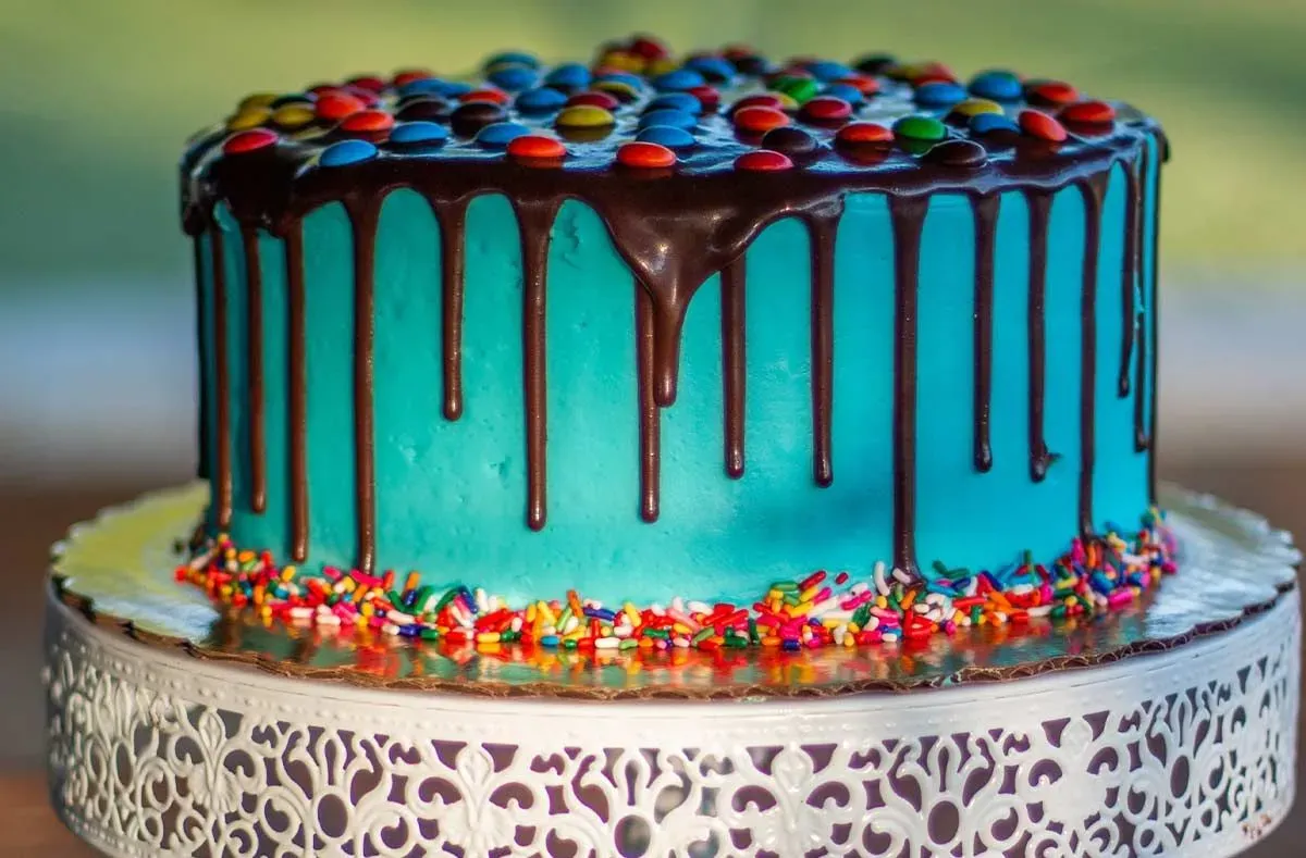 Blue iced cake with melted chocolate dripping down the sides, Smarties on top.