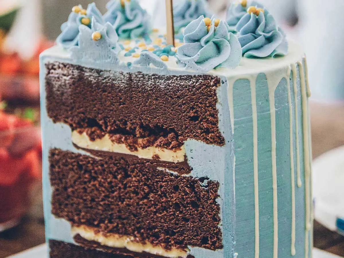 Tiered cake with blue frosting cut revealing the chocolate sponge inside.