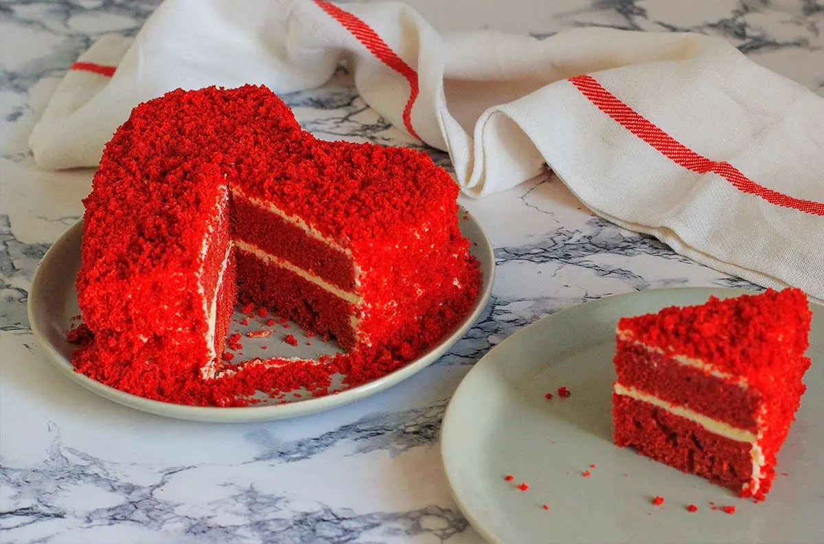 Red heart shaped red velvet cake with cake crumbled on top of the frosting.