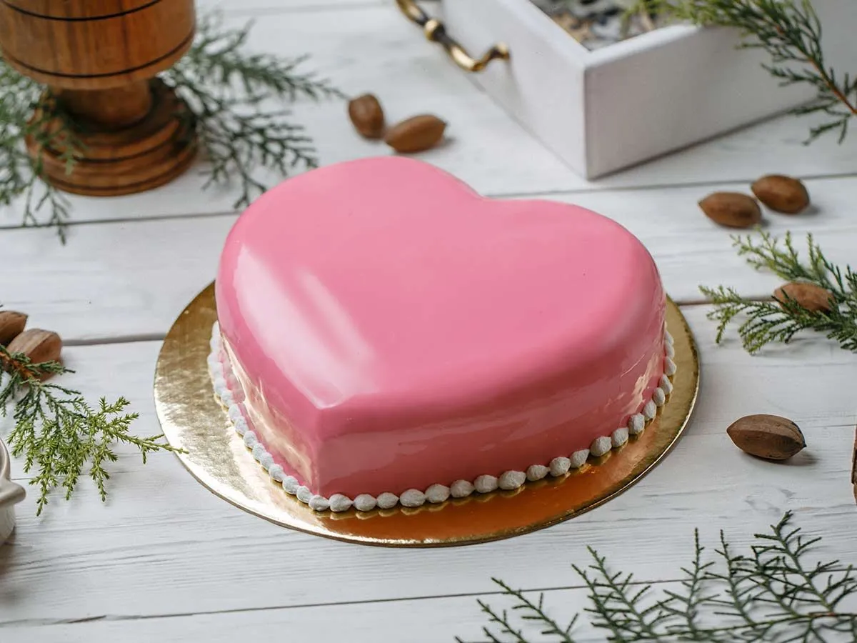 Pink heart shaped cake on a gold cake board.