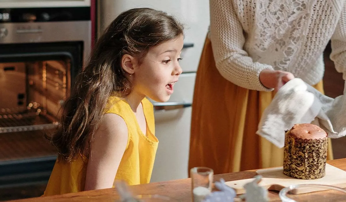 Little girl in the kitchen amazed at a chocolate cake her mum is taking out the oven.