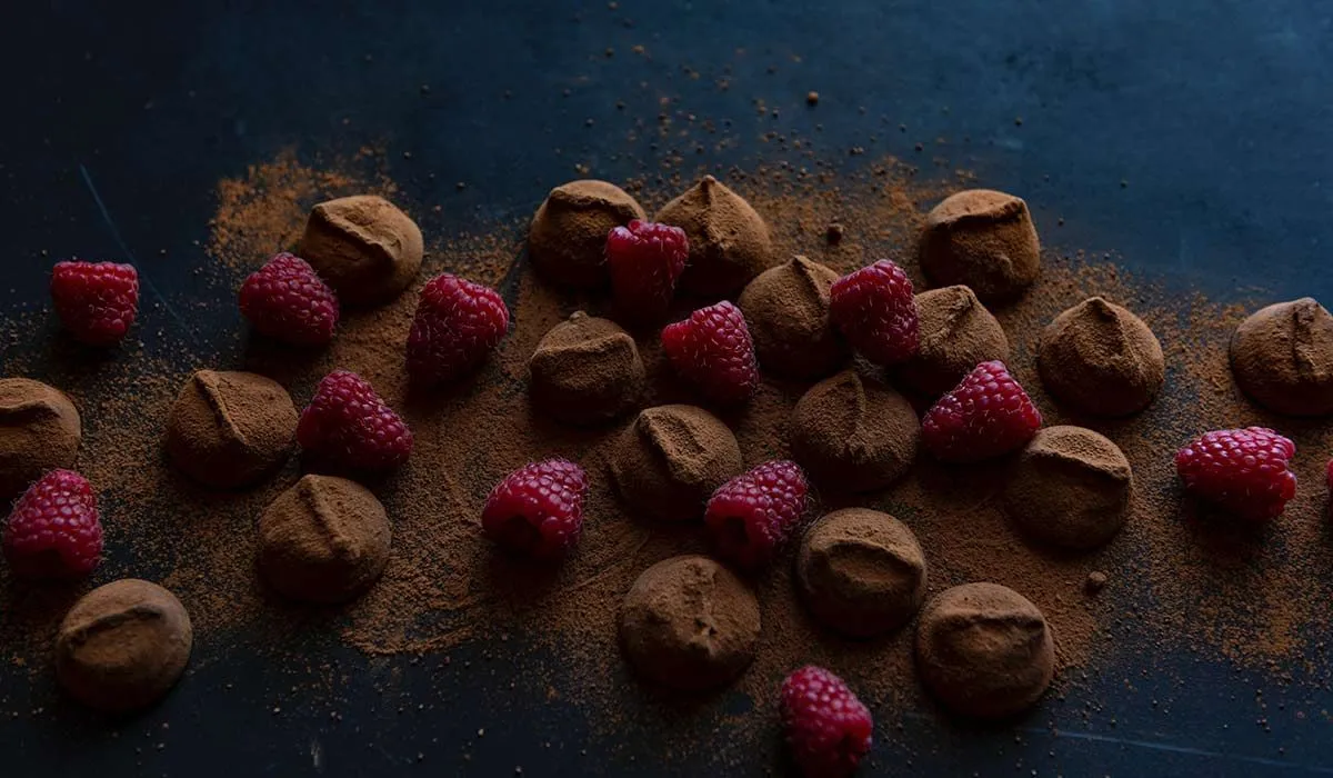 Chocolate truffles dusted with cocoa powder and raspberries.