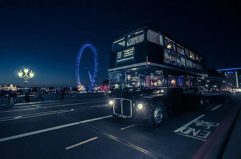 The Ghost Bus Tour Routemaster bus driving through London at night with the London Eye in the background.