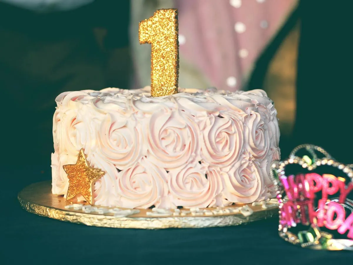 Birthday cake with light pink rose swirl icing and a gold number one candle on top.