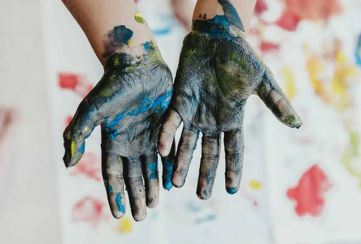 Hands, palms facing up, covered in blue and yellow paint from stamp making.