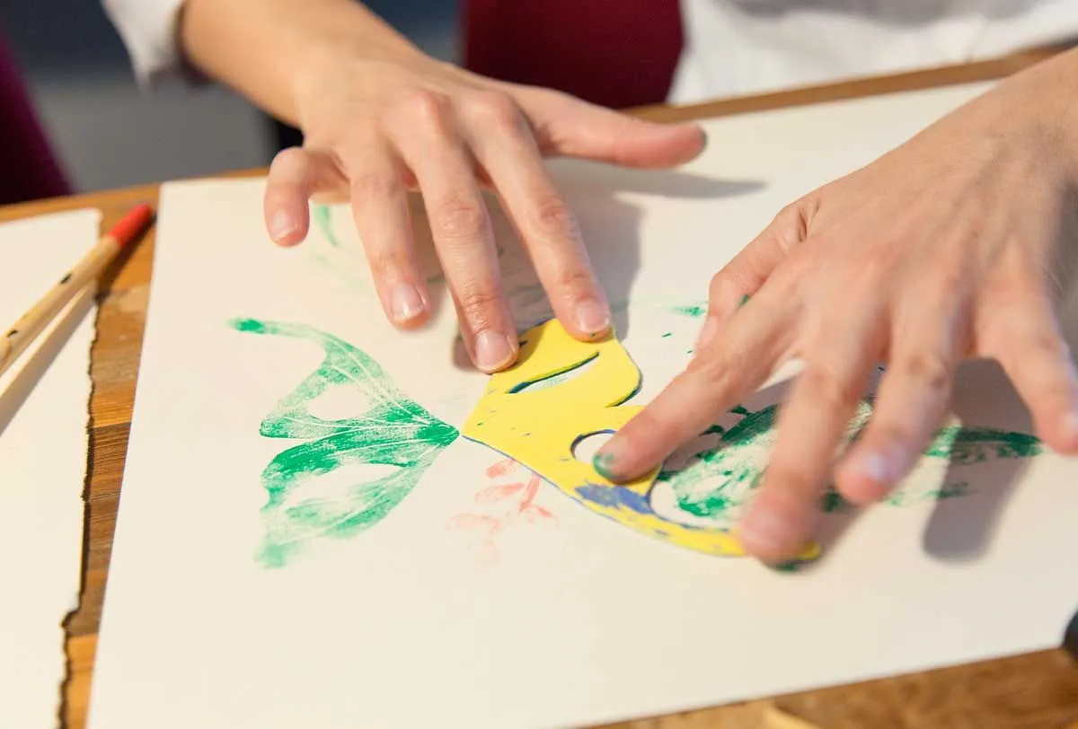 Close up of a person's hands as they use a stamp to paint a green butterfly.