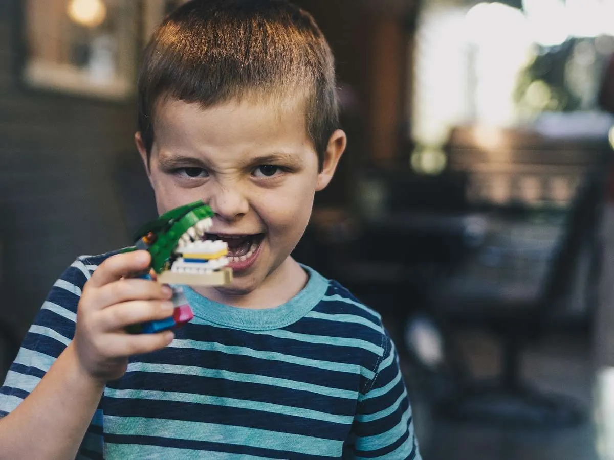 Young boy playing with a dinosaur toy making a face as if he's roaring.