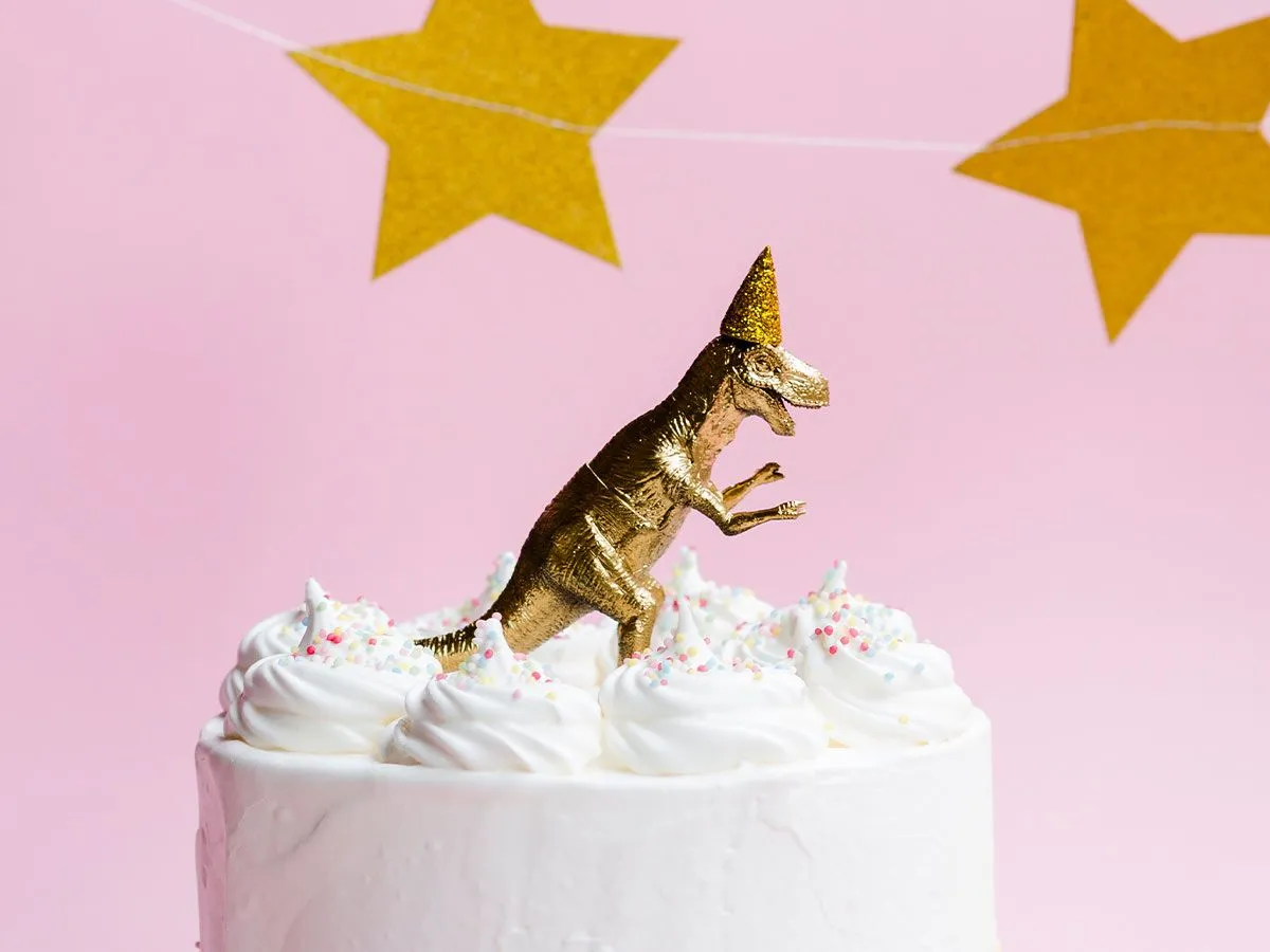 White cake with a gold dinosaur toy model on top.