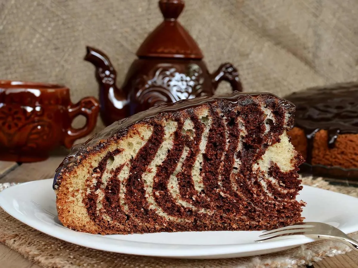 A slice of zebra cake with chocolate glaze.