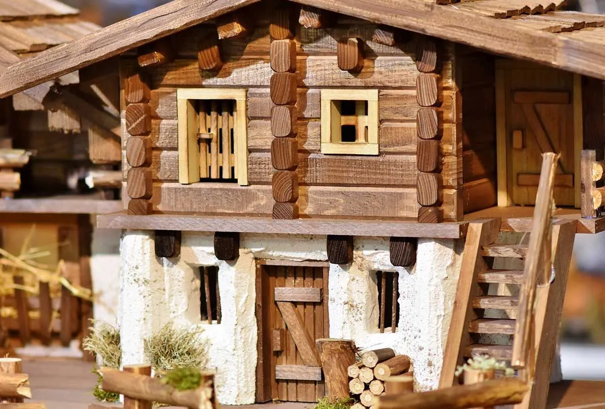 A model wooden house with a rack of logs by the front door and stairs to the upper floor.