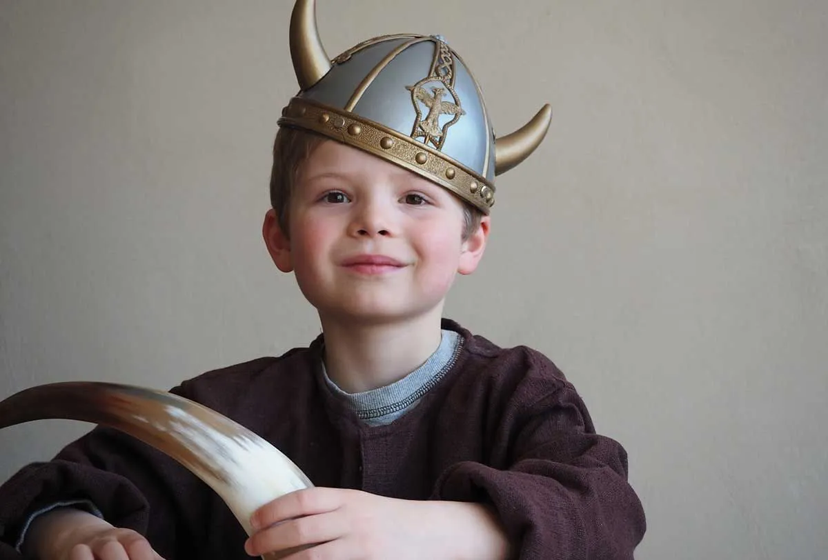 Young boy wearing a Viking helmet on his head smiling.