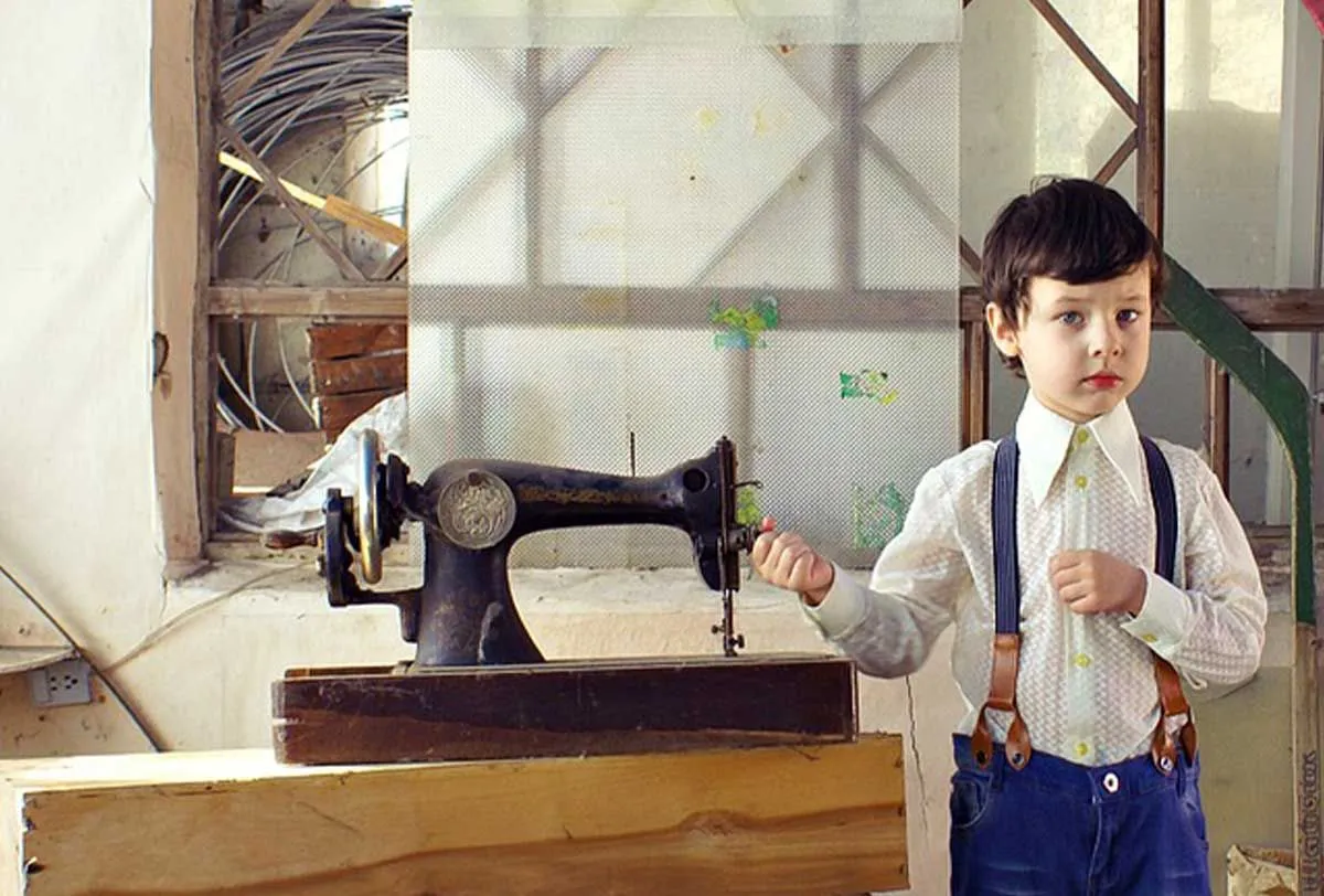 Young boy standing next to an old-fashioned sewing machine.