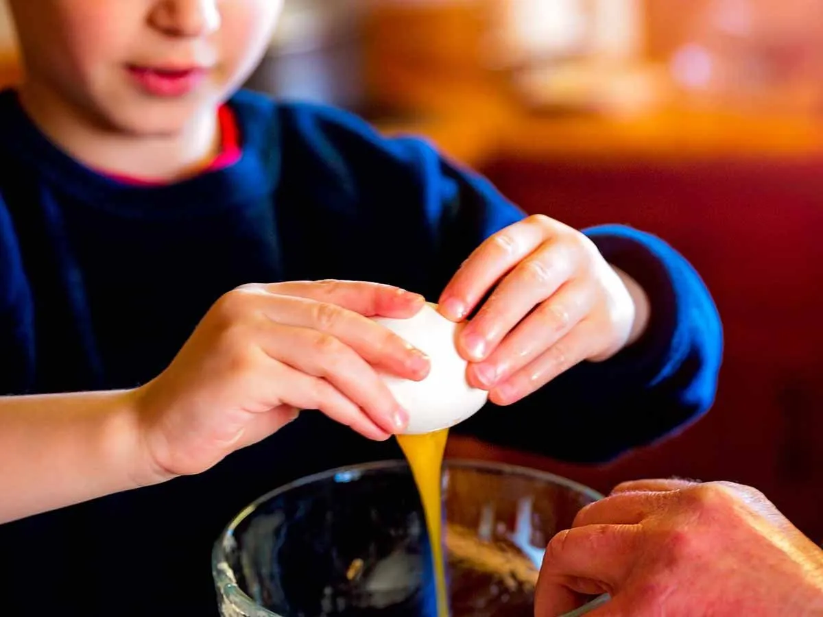 Close up of a boy cracking an egg into a bowl to make a pizza cake.