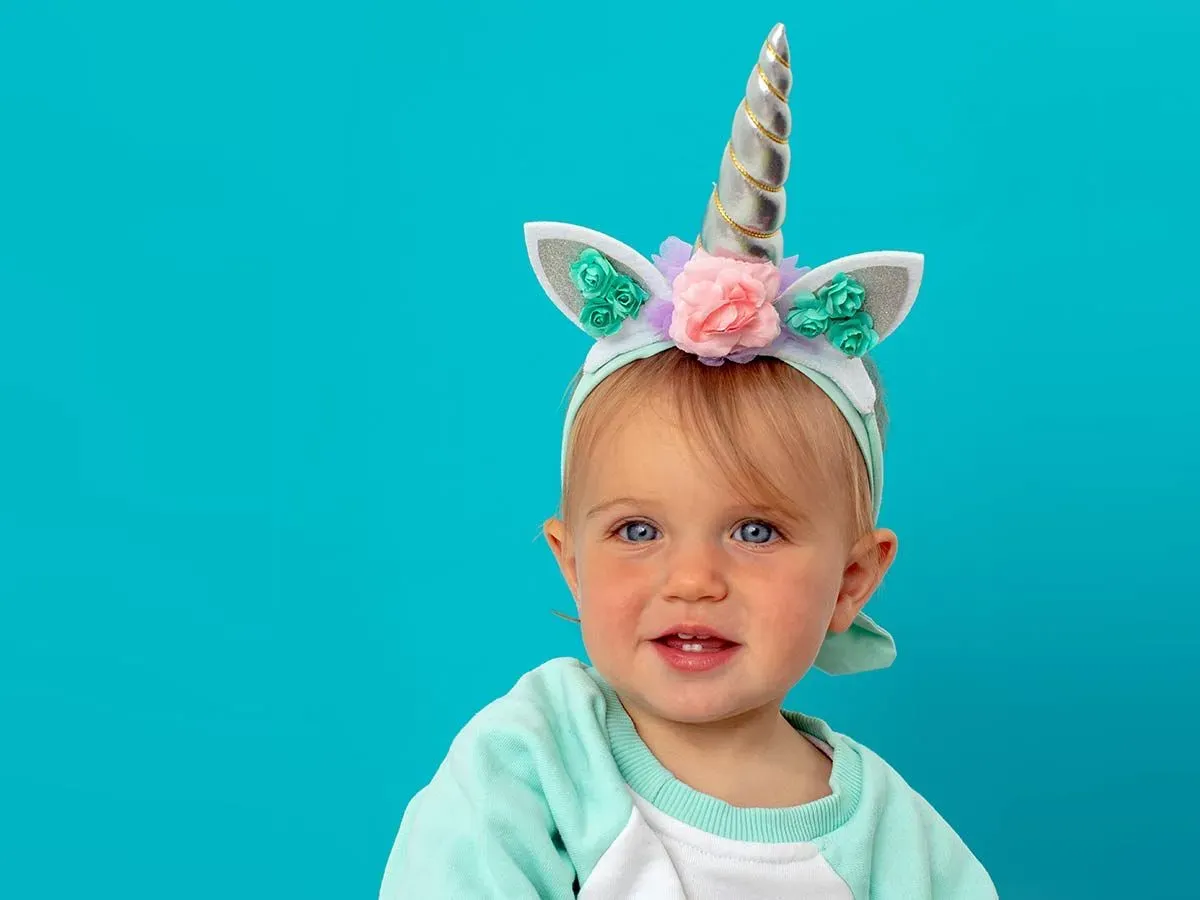 Toddler sat in front of a blue background wearing a DIY unicorn horn.