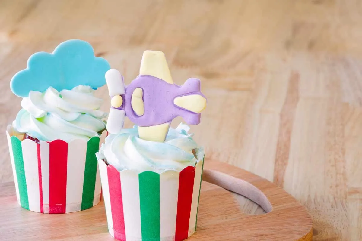 Cupcakes with a decorative, icing airplane stuck in one and an icing cloud in the other.