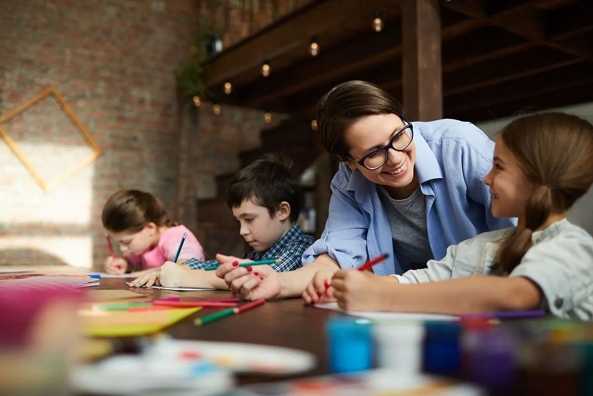 Kids sat at table making DIY chore charts, their mum smiling at the girl sat at the front.