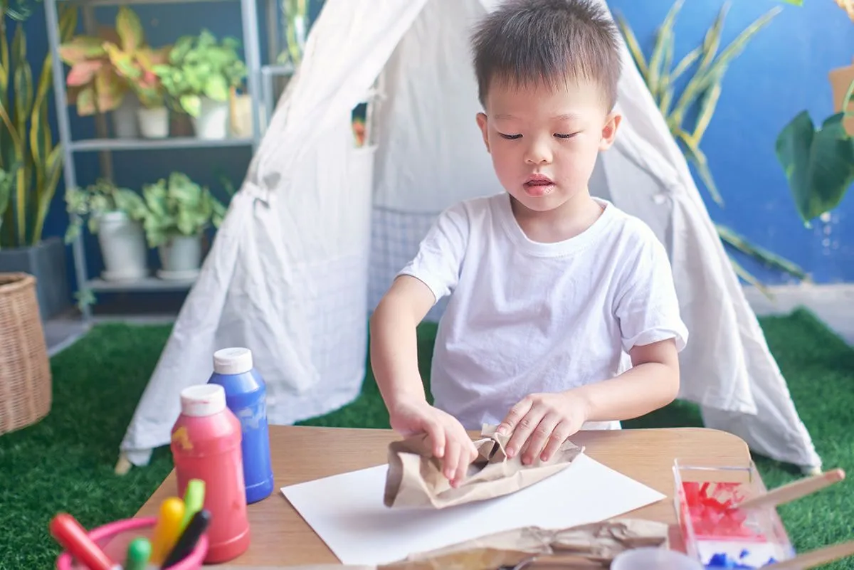 Young boy sat by a table in front of a living-room tent making a DIY chore chart.