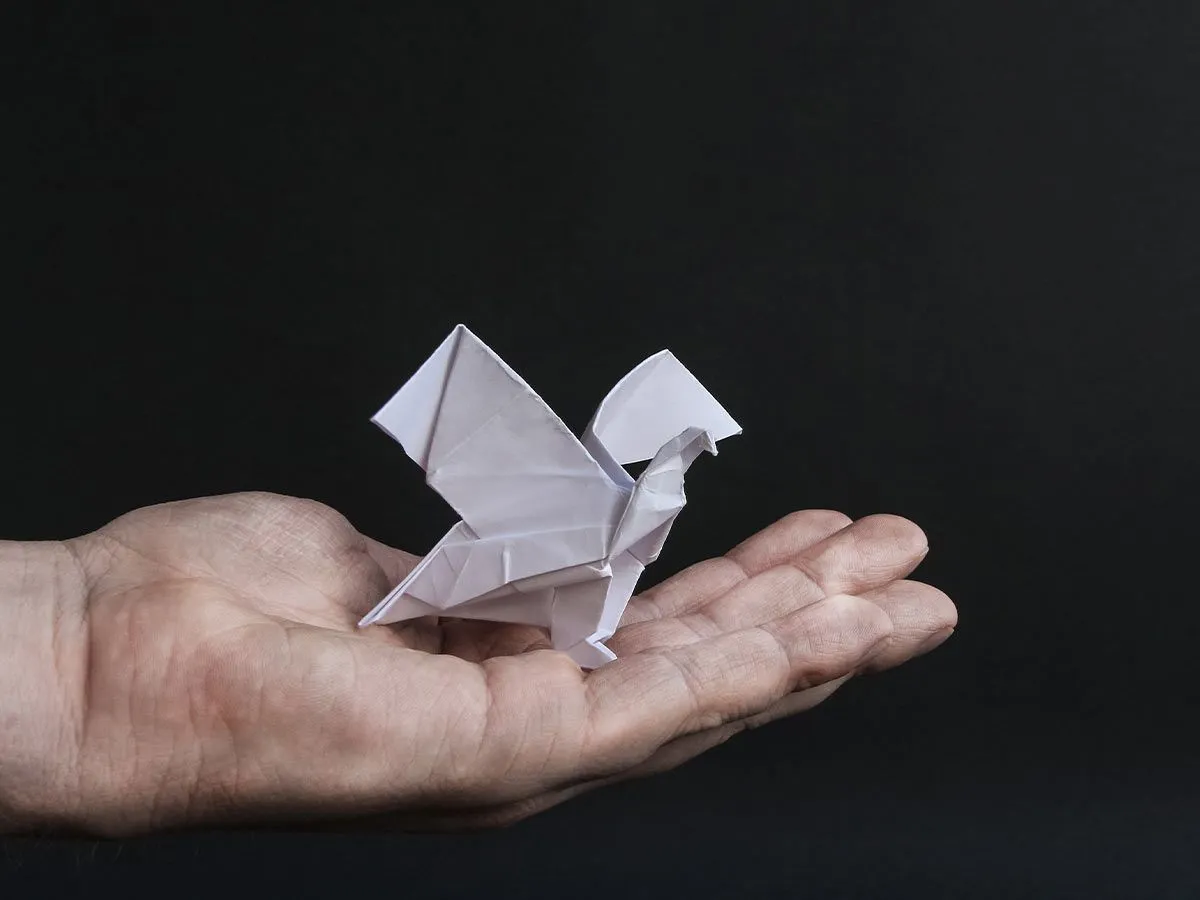A white origami eagle in the open palm of a hand against a black background.