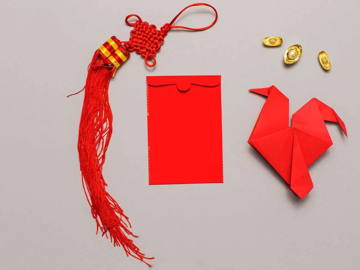 Red origami eagle on the surface next to a red envelope and tassel.