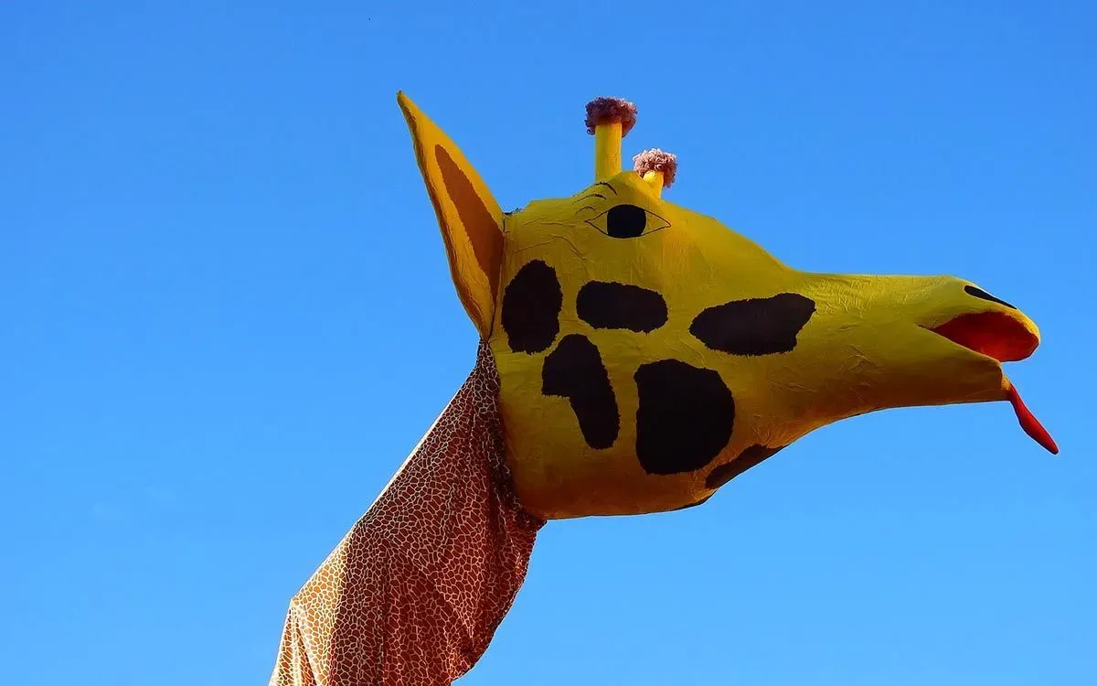A large paper mache giraffe head with a blue sky in the background.