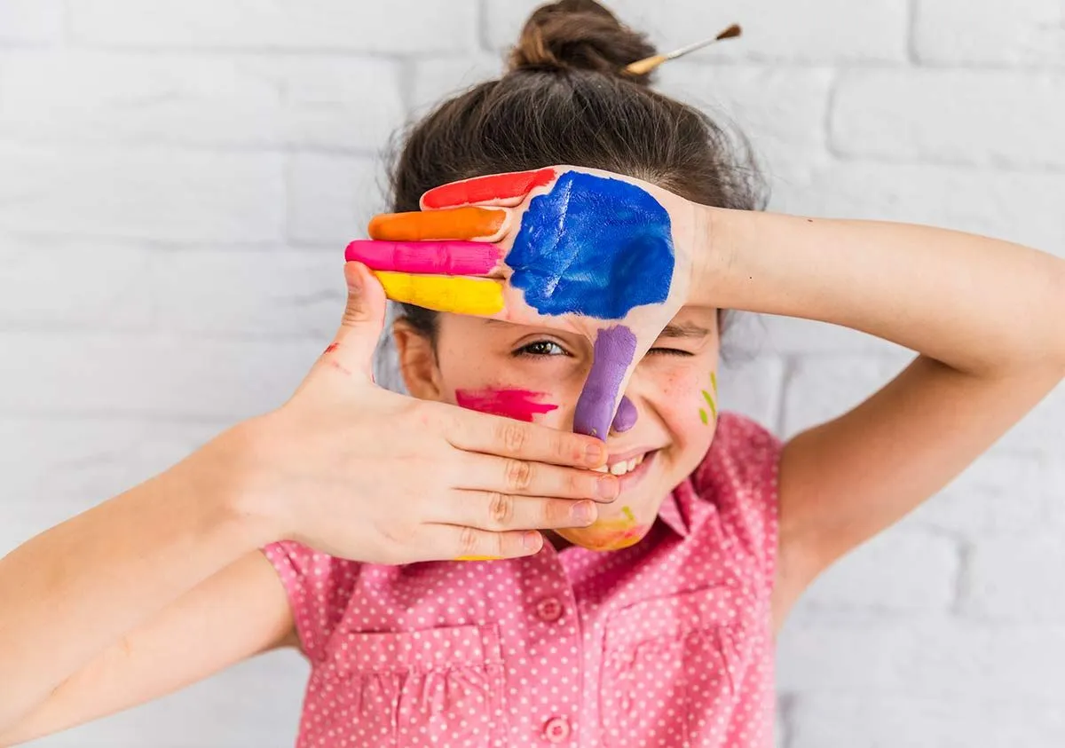 Young girl with paint on her hands making a sign framing her eye.