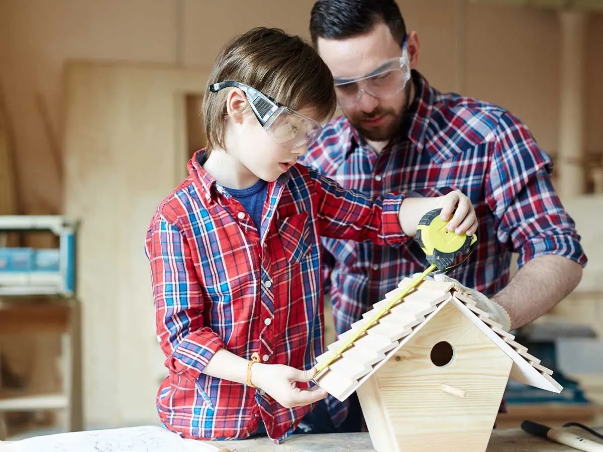 Father and son checking that their bird box is correct with a measuring tape.