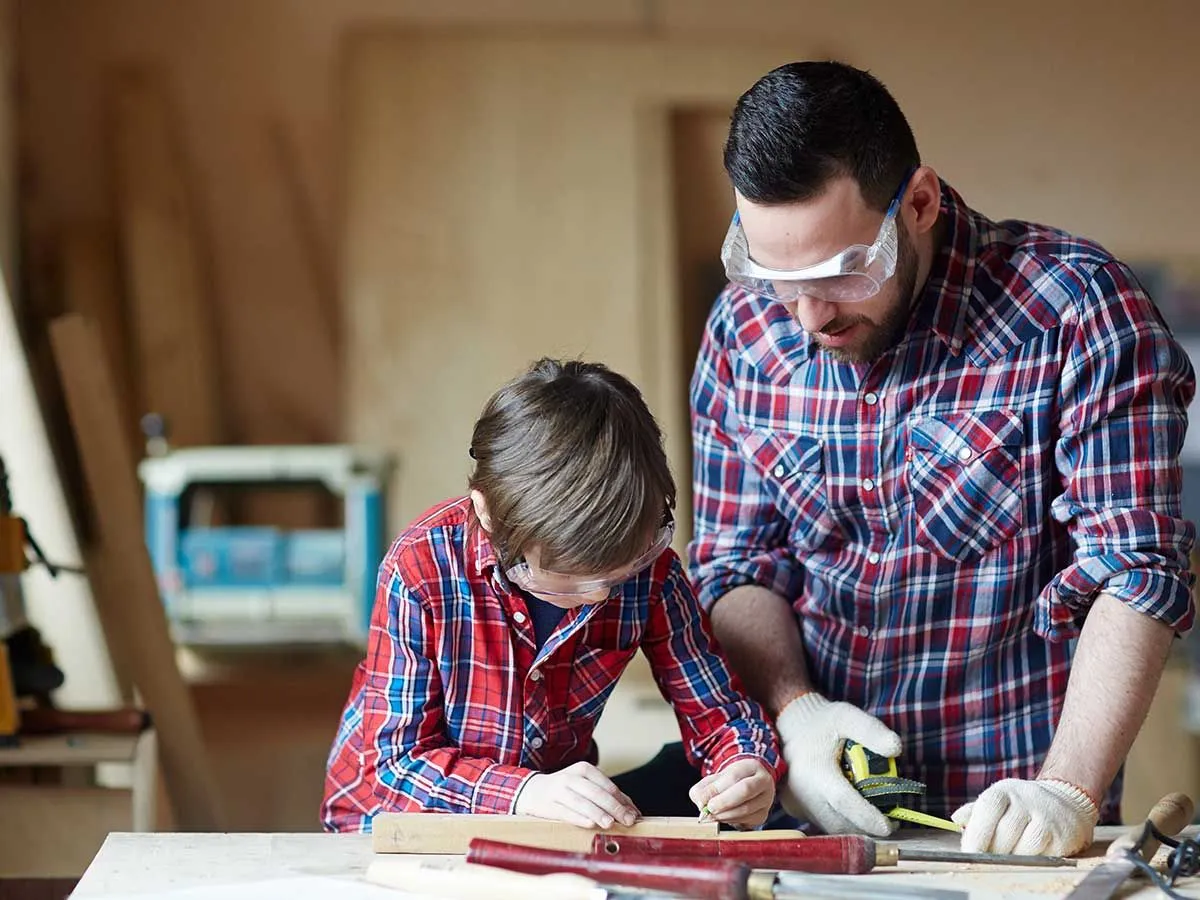 Father and son measuring the pieces of wood they need to make a bird box.