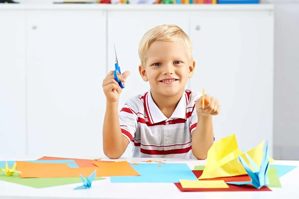 Boy smiling as he holds scissors and paper ready to make an origami bear.
