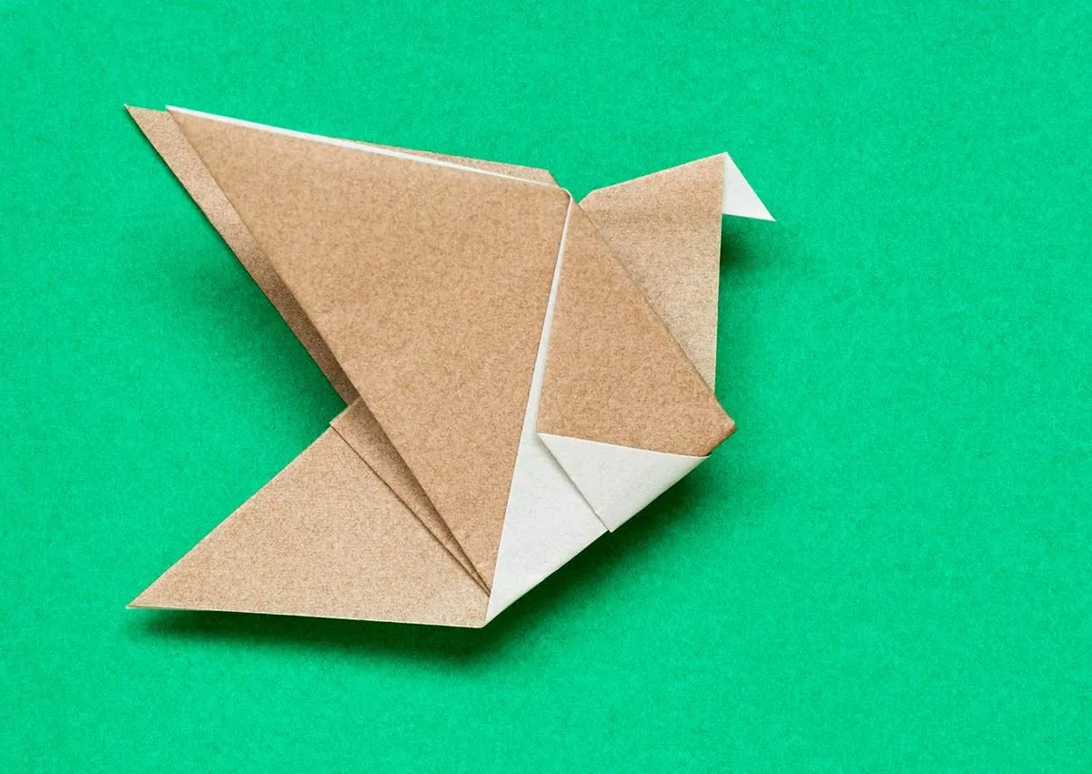 A brown and white origami robin lying on a green background.