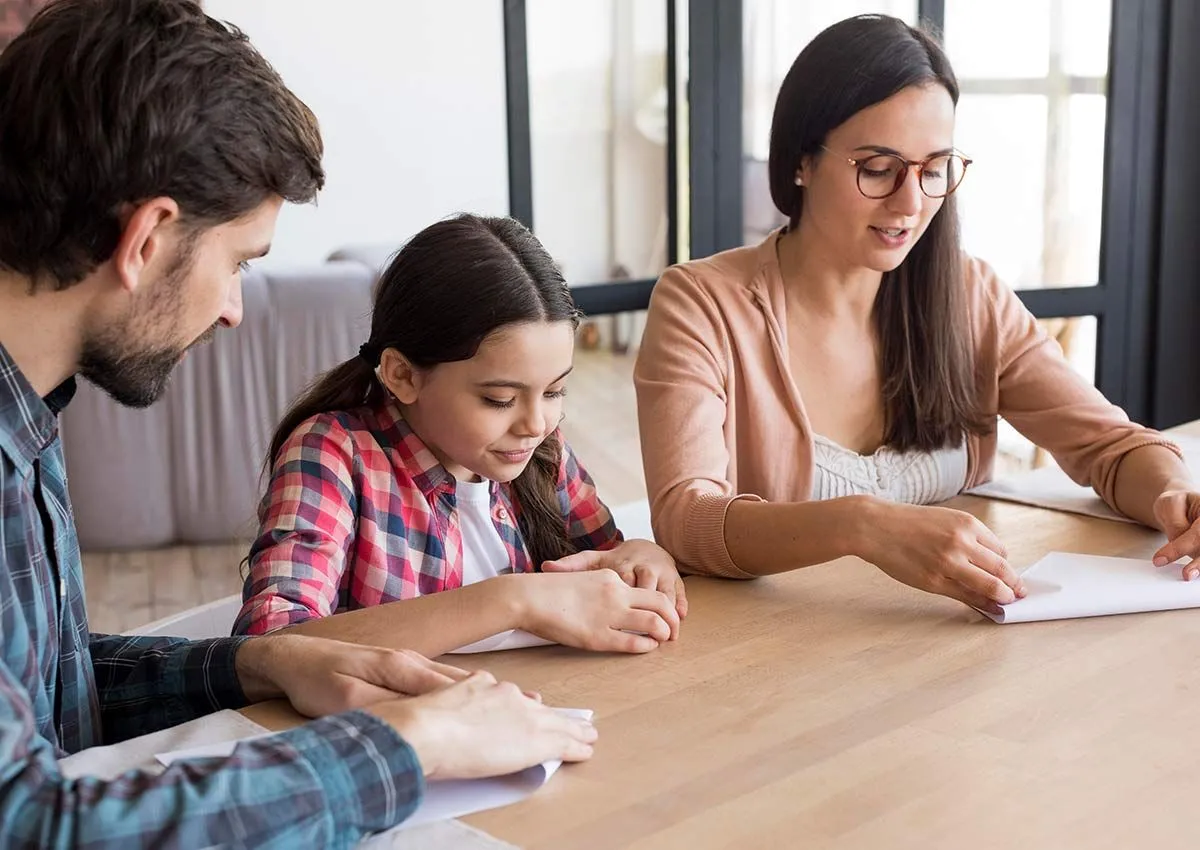 Girl and her parents sat at the table together folding a piece of paper each to make an origami robin.