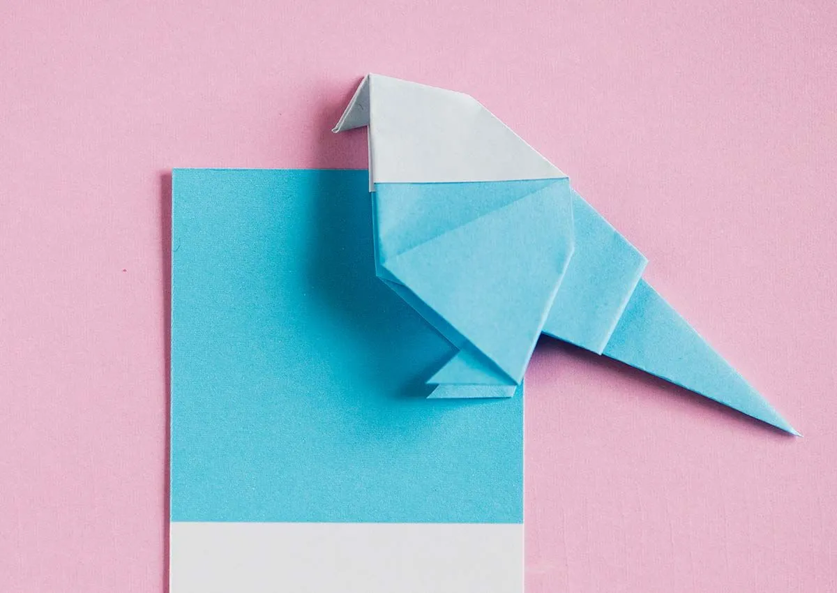 Blue and white origami robin against a light pink background.